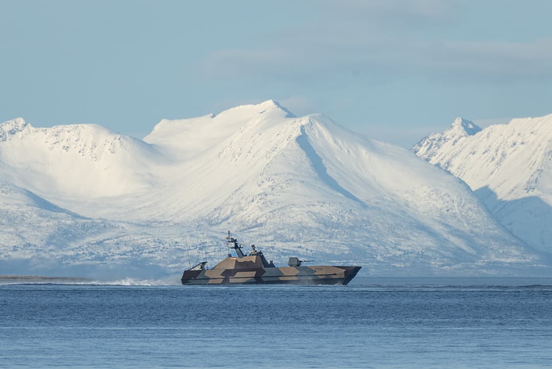 Fartøy på kaldt hav foran snødekte fjell.
